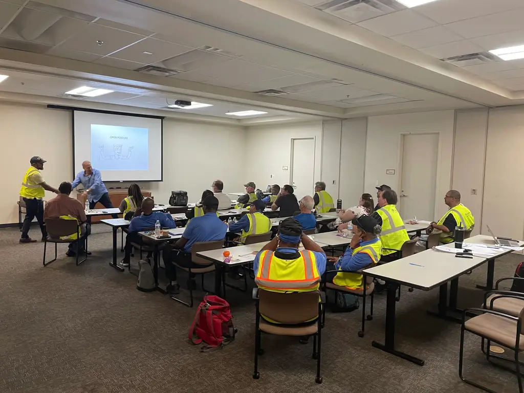 Transit operators in high visibility vests seated through an RWC Training session, an OPEN POSTURE slide on the screen